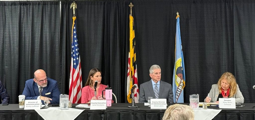 County and state officials at the head table of the Wicomico legislative breakfast at the Civic Center, with the American, Maryland and Wicomico flags behind them.